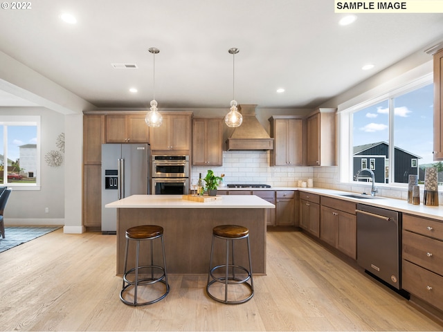 kitchen with a breakfast bar, sink, hanging light fixtures, stainless steel appliances, and wall chimney range hood