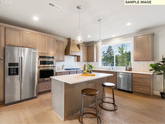 kitchen featuring premium range hood, hanging light fixtures, a kitchen island, stainless steel appliances, and light hardwood / wood-style floors