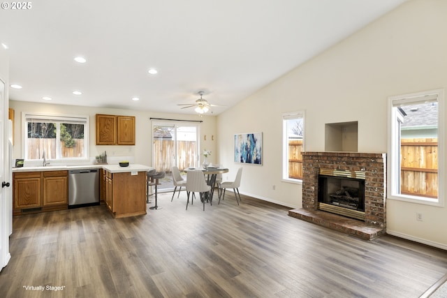 kitchen with light countertops, brown cabinetry, open floor plan, dishwasher, and a peninsula