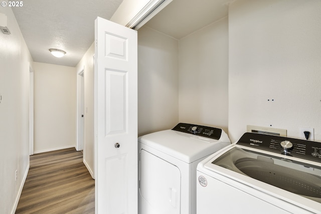 clothes washing area with a textured ceiling, laundry area, wood finished floors, baseboards, and washer and dryer