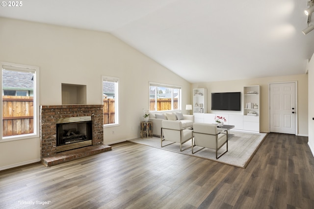 living room with a brick fireplace, vaulted ceiling, baseboards, and wood finished floors