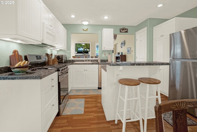 2146 NW Jetty Ave, Lincoln City, OR 97367 - kitchen with appliances with stainless steel finishes, a sink, a breakfast bar, light wood-style flooring, and white cabinetry