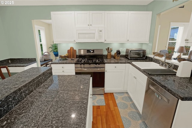 2146 NW Jetty Ave, Lincoln City, OR 97367 - kitchen with appliances with stainless steel finishes, a sink, light wood-type flooring, white cabinets, and a peninsula