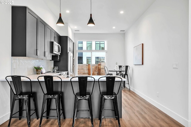 kitchen with hanging light fixtures, kitchen peninsula, a kitchen bar, gray cabinets, and decorative backsplash