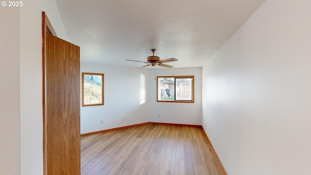 empty room with ceiling fan, a wealth of natural light, a textured ceiling, and light hardwood / wood-style floors