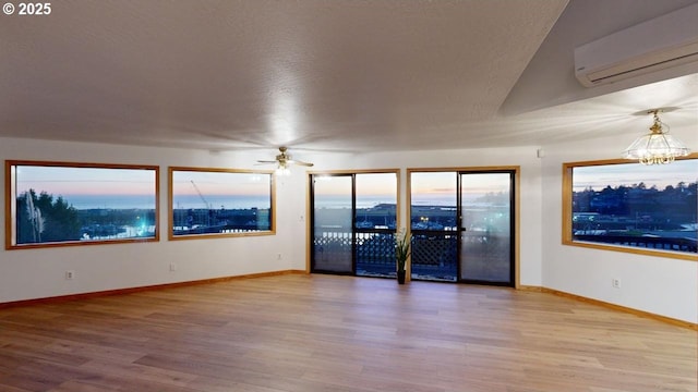 unfurnished room with hardwood / wood-style flooring, ceiling fan with notable chandelier, a textured ceiling, and a wall unit AC