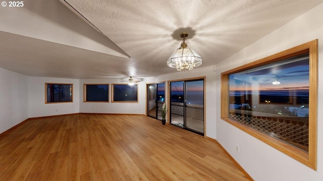 empty room featuring wood-type flooring, ceiling fan with notable chandelier, and a textured ceiling