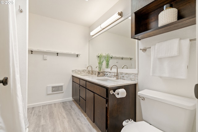 bathroom with wood finished floors, toilet, double vanity, tasteful backsplash, and baseboards