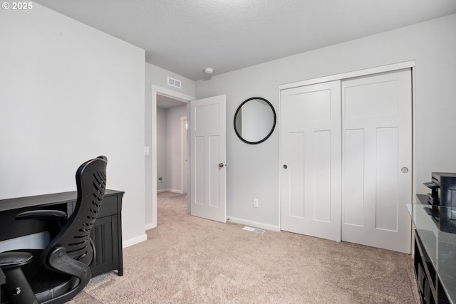 home office featuring a textured ceiling, baseboards, visible vents, and light carpet