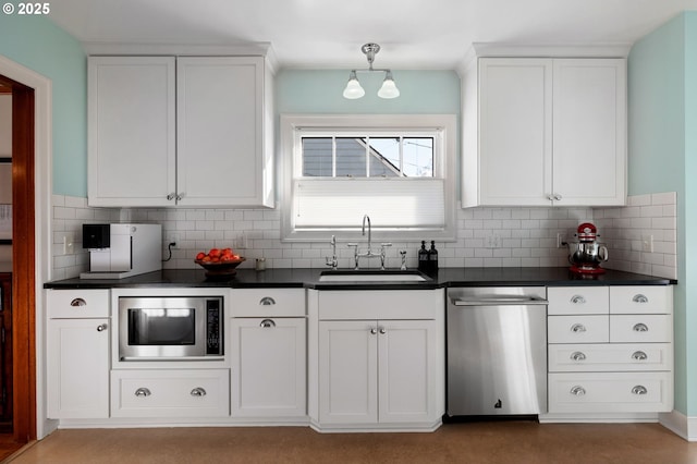 kitchen with stainless steel appliances, dark countertops, decorative backsplash, white cabinets, and a sink