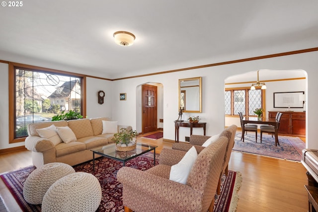 living area featuring arched walkways, ornamental molding, and light wood-type flooring