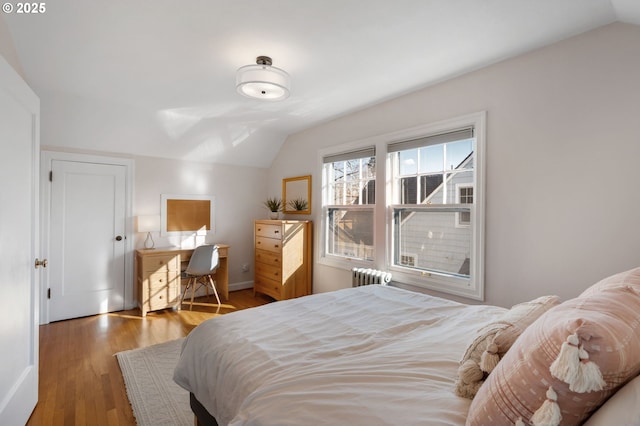 bedroom with vaulted ceiling, radiator heating unit, and wood finished floors