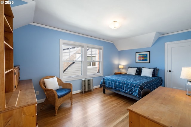 bedroom with lofted ceiling, light wood-style floors, baseboards, and radiator