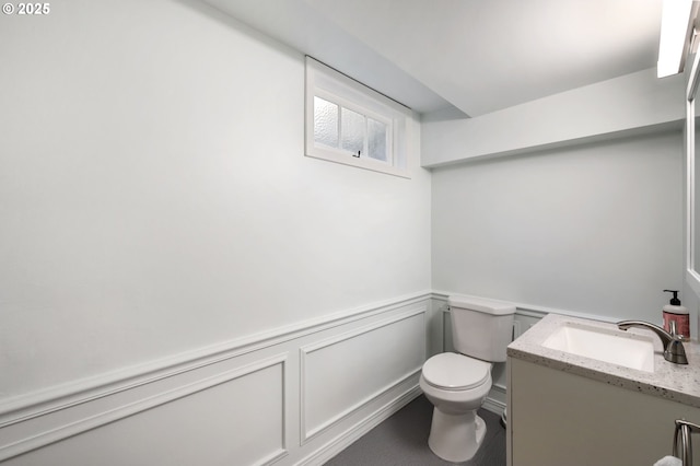 half bath featuring toilet, a wainscoted wall, and vanity