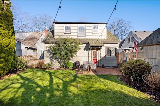 rear view of house featuring a patio, a shingled roof, a lawn, and fence