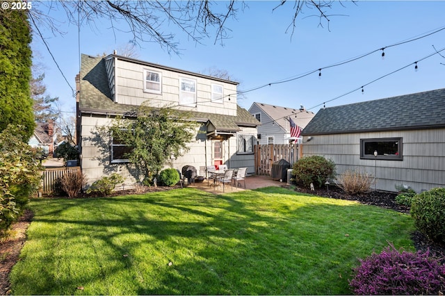 back of property featuring a shingled roof, a patio area, fence, and a lawn