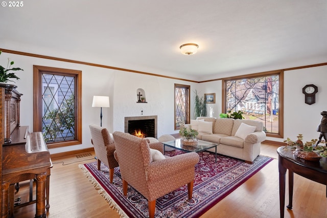 living room with light wood-type flooring, crown molding, a lit fireplace, and baseboards