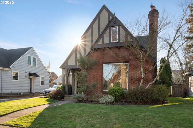 tudor home with a chimney, a front lawn, and brick siding