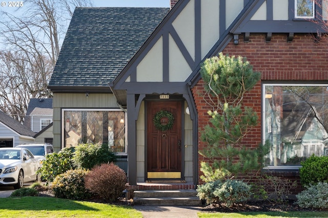 doorway to property with stucco siding, roof with shingles, a chimney, and brick siding