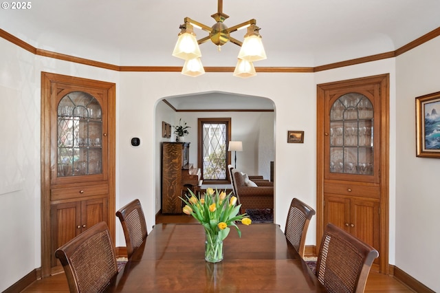 dining area featuring arched walkways, crown molding, baseboards, and wood finished floors