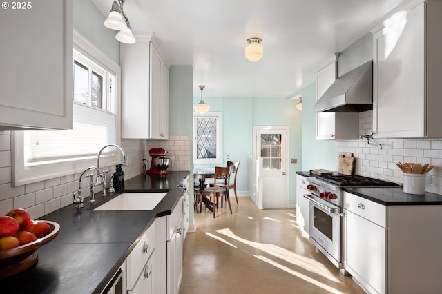 kitchen featuring white cabinets, dark countertops, high end range, wall chimney range hood, and a sink