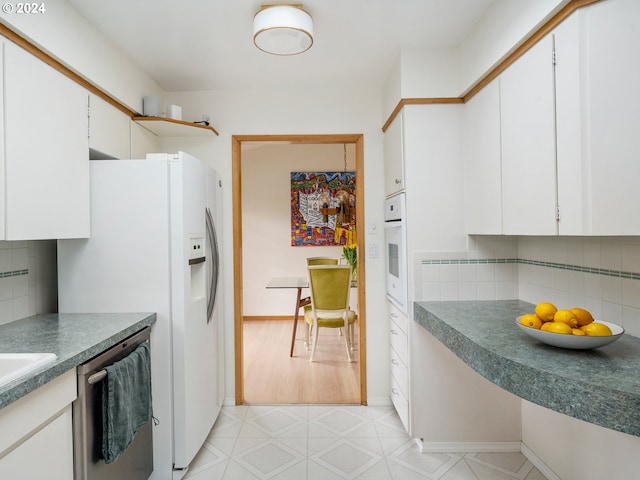 kitchen featuring light floors, dark countertops, decorative backsplash, white cabinets, and white appliances