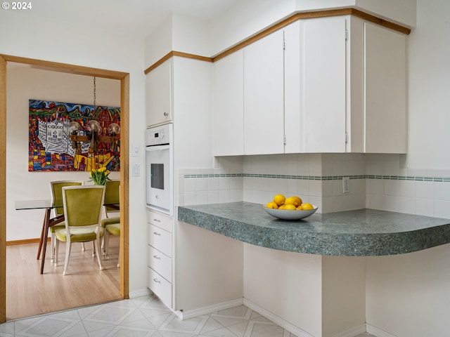 kitchen featuring dark countertops, backsplash, oven, and white cabinets