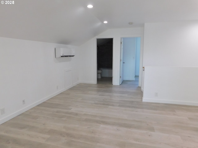 additional living space featuring light hardwood / wood-style flooring, an AC wall unit, and vaulted ceiling