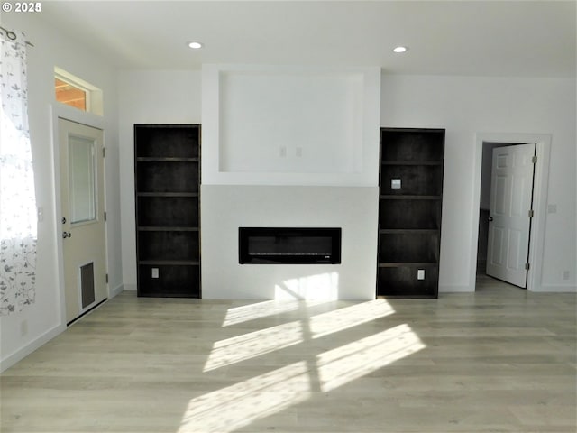 unfurnished living room featuring built in features and light hardwood / wood-style floors