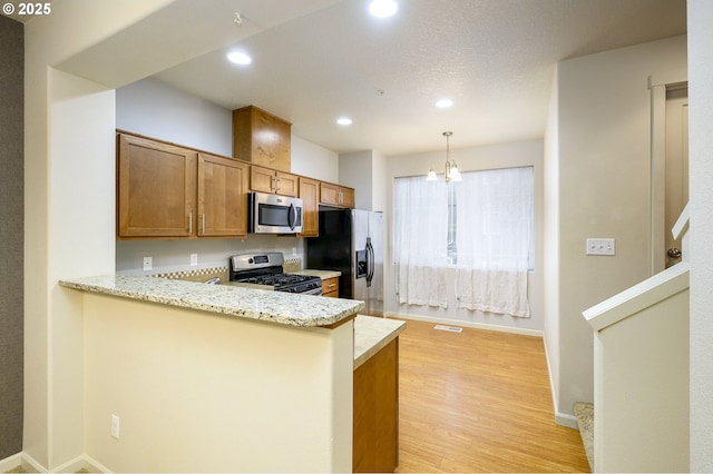 kitchen with light stone countertops, an inviting chandelier, kitchen peninsula, appliances with stainless steel finishes, and light wood-type flooring