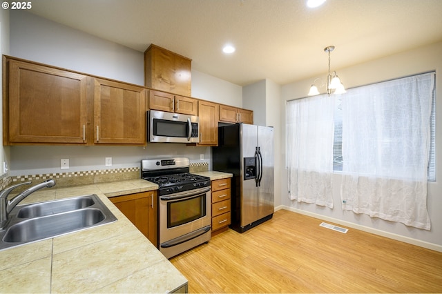 kitchen with stainless steel appliances, sink, light hardwood / wood-style flooring, a notable chandelier, and hanging light fixtures