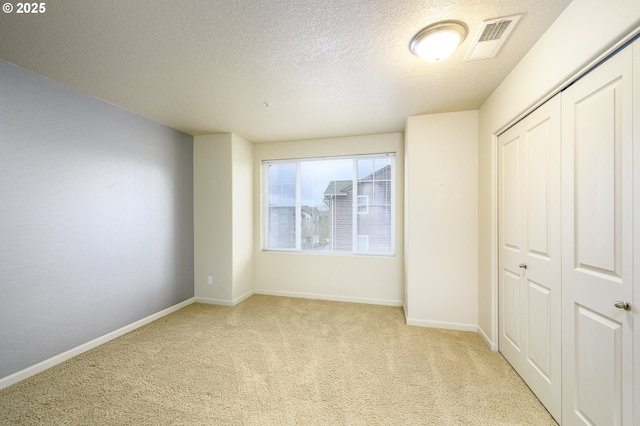 unfurnished bedroom with light carpet, a closet, and a textured ceiling