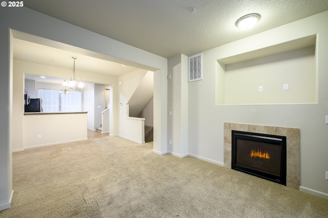 unfurnished living room featuring light colored carpet, a textured ceiling, a tile fireplace, and a chandelier