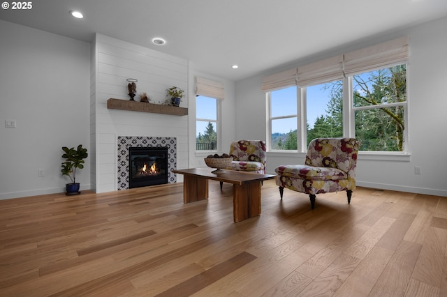 living room featuring light wood-style flooring, a tiled fireplace, baseboards, and recessed lighting