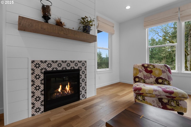 living area with baseboards, plenty of natural light, wood finished floors, and a tile fireplace