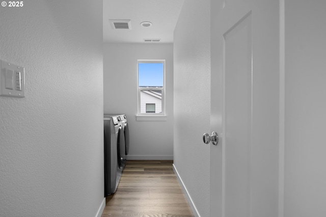 hall featuring visible vents, washing machine and dryer, light wood-style floors, baseboards, and a textured wall