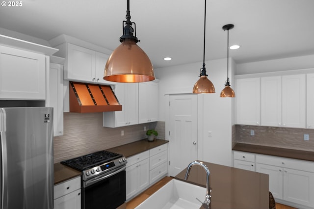 kitchen with dark countertops, range hood, appliances with stainless steel finishes, and white cabinets