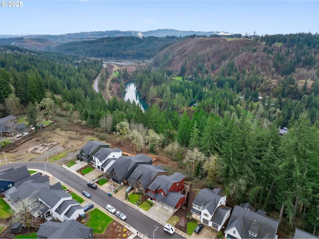 aerial view of property and surrounding area featuring a mountain backdrop, a forest, and nearby suburban area
