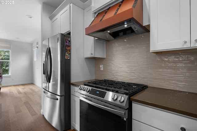 kitchen with custom exhaust hood, appliances with stainless steel finishes, white cabinetry, dark countertops, and tasteful backsplash