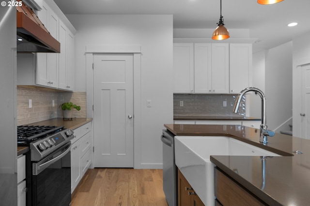 kitchen featuring under cabinet range hood, dishwasher, light wood-style floors, gas stove, and white cabinetry