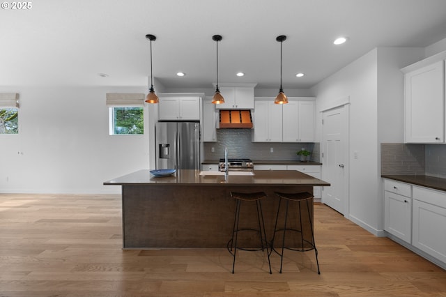 kitchen with stainless steel appliances, dark countertops, a sink, backsplash, and white cabinetry