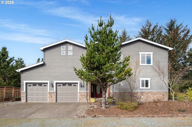 view of front of home with stone siding, an attached garage, concrete driveway, and fence