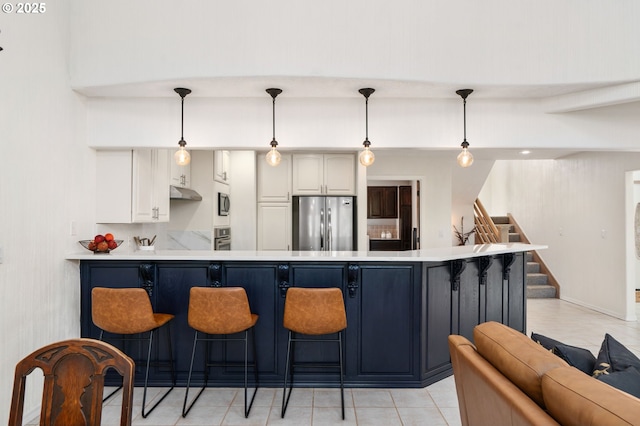 kitchen with a peninsula, stainless steel appliances, light countertops, under cabinet range hood, and a kitchen breakfast bar