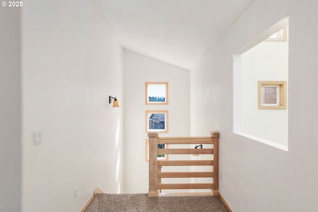 corridor with an upstairs landing, carpet, and vaulted ceiling