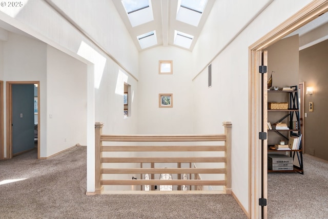 hallway with carpet floors, an upstairs landing, and vaulted ceiling with skylight