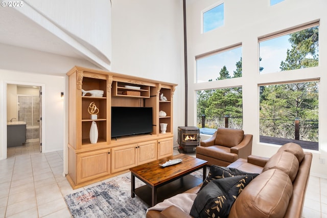 living room featuring a wealth of natural light, a towering ceiling, a wood stove, and light tile patterned floors