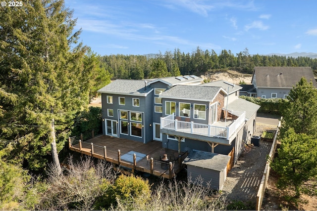 rear view of property featuring central air condition unit, a shingled roof, a wooden deck, and a view of trees