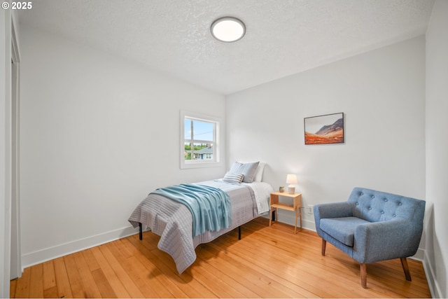 bedroom with baseboards, light wood-type flooring, and a textured ceiling