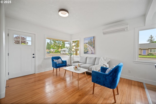 living room with an AC wall unit, baseboards, wood-type flooring, and a textured ceiling