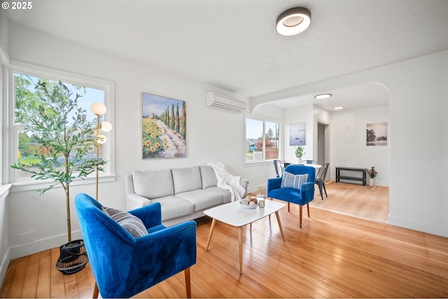 living room with a wall mounted AC, wood finished floors, arched walkways, and baseboards